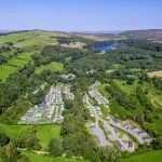 aerial photo of holiday park surrounded by trees and rolling green hills with a glimmering lake in the distance